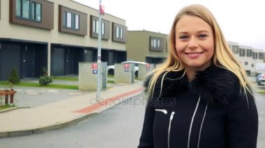 Genç, güzel bir kadın hemen dışında sokakta duruyor ve bize onun arkasında binalar sunar