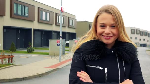 Une jeune et belle femme se tient à l'arrière de la caméra dans une banlieue, puis tourne, plie les bras sur sa poitrine et sourit à la caméra — Video