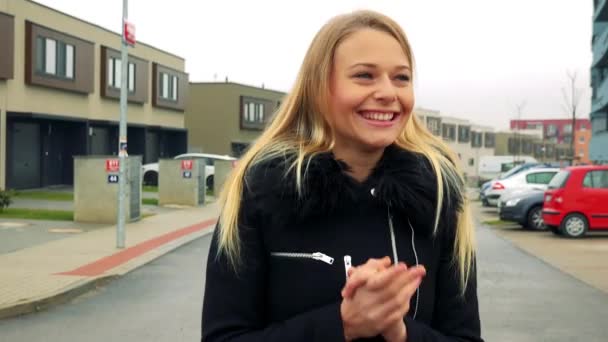 Молодая, привлекательная женщина стоит на улице в пригородном районе и празднует, здания на заднем плане — стоковое видео