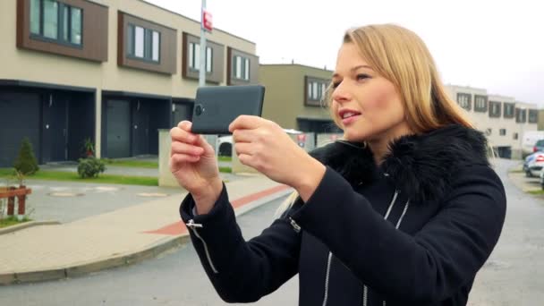 Una giovane e bella donna si trova per strada in una zona periferica e scatta una foto con uno smartphone — Video Stock