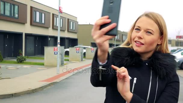 A young, beautiful woman stands on the street in a suburban area and takes a selfie with a smartphone — Stock Video