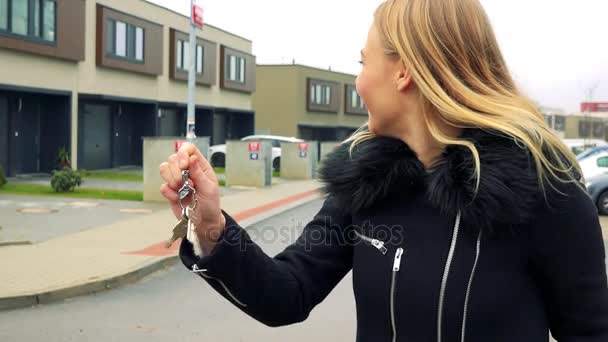 Młoda, piękna kobieta stoi na ulicy w strefie podmiejskiej, uśmiecha się do kamery i Clinks dysponuje miejscem klucze w ręku — Wideo stockowe