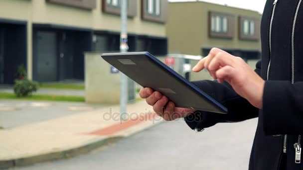 Una mujer está parada en la calle en una zona suburbana y trabaja en una tableta - una calle en el fondo — Vídeos de Stock