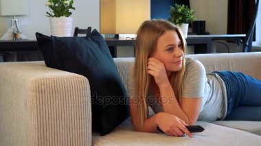 Genç, güzel bir kadın bir oturma odasında kanepede yatıyor ve kamera kapalı olan bir TV kanalları geçer