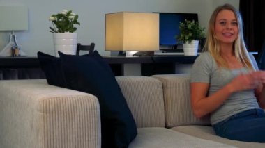 Genç, güzel bir kadın bir kanepe oturma odasında oturur ve kameraya konuşuyor