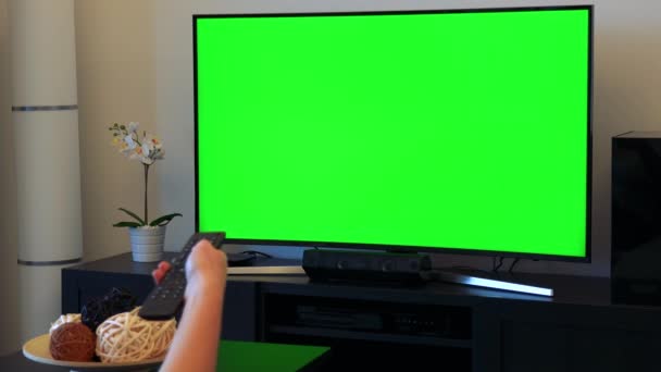 Una mujer cambia de canal en un televisor con pantalla verde — Vídeos de Stock