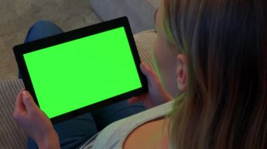 Sarışın bir kadın kanepede oturur ve bir tablet vasıl onun elinde yeşil bir ekran görünüyor