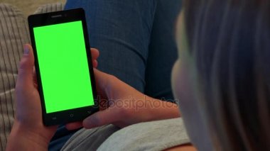 Sarışın bir kadın kanepede oturur ve bir smartphone vasıl onun elinde - portre ile yeşil bir ekran görünüyor