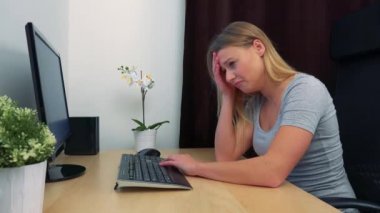 Genç, güzel bir kadın bir bilgisayar önünde bir masada oturur ve hayal kırıklığı görüntüler