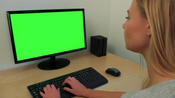 Una mujer joven se sienta en un escritorio y trabaja en una computadora con una pantalla verde — Vídeos de Stock