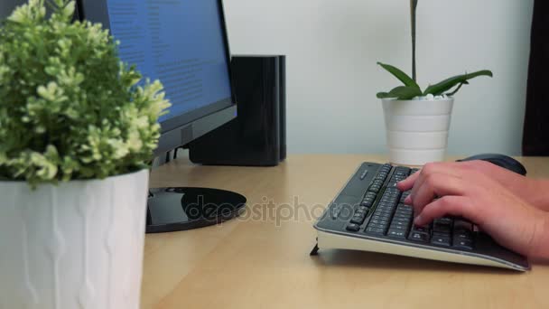 Una mujer se sienta en un escritorio frente a una pantalla de computadora y escribe en un teclado — Vídeos de Stock