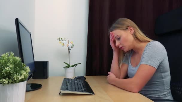 Μια νεαρή, όμορφη γυναίκα κάθεται σε ένα γραφείο μπροστά από έναν υπολογιστή και παίρνει τον αναστατώσει — Αρχείο Βίντεο