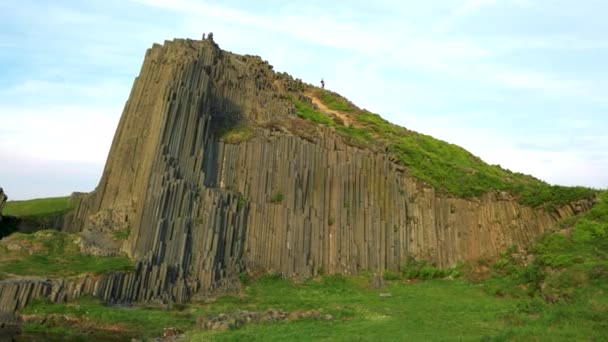 Uma rocha colunar de basalto perto de um lago, o céu azul brilhante no fundo — Vídeo de Stock