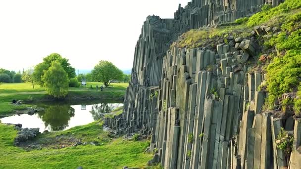 Ein säulenförmiger Basaltfelsen, der in der Nähe eines Sees mit Büschen bewachsen ist — Stockvideo
