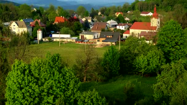 Malá vesnička obklopená stromy, mountainious krajina na pozadí - pohled shora — Stock video