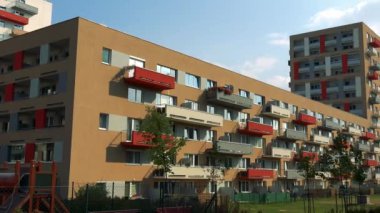 Renkli (kırmızı, sarı, gri) balkon, arka plan, çim ve ağaçların ön planda parlak mavi gökyüzünde ile bej bir apartman