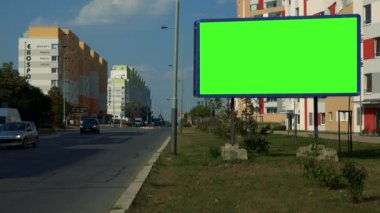 Bir kentsel alanda, arabalar geçip, renkli apartman binaları ve açık mavi gökyüzü arka planda bir karayoluyla yeşil bir ekran ile bir Pano