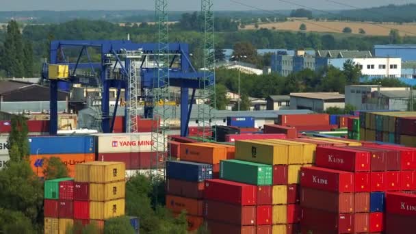 Ein Kran fährt durch einen Hof aus bunten Containern, im Hintergrund ein riesiges ländliches Gebiet - Draufsicht — Stockvideo