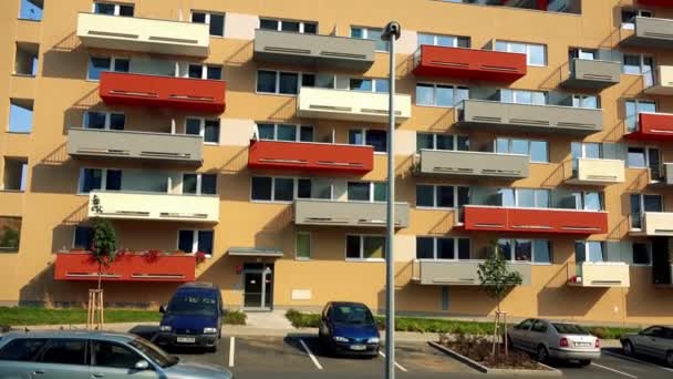 A beige apartment building with colorful (red, yellow, gray) balconies in an urban area, the blue sky in the background, a carpark in the foreground — Stock Video