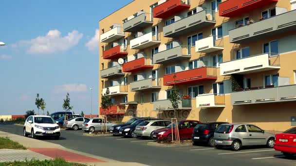 A beige apartment building with colorful (red, yellow, gray) balconies in an urban area, the blue sky in the background, a carpark in the foreground — Stock Video