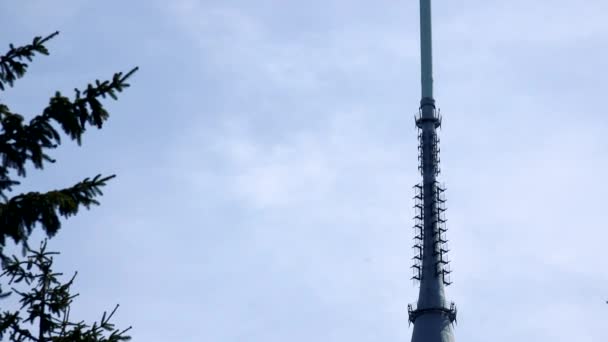 Un'alta torre televisiva bianca dal basso, il cielo azzurro brillante sullo sfondo, gli alberi in primo piano — Video Stock