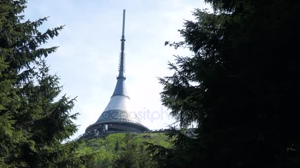 높은 흰색 텔레비전 타워 아래에서 백그라운드에서 밝은 푸른 하늘 나무 전경 — 비디오