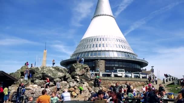 Folk sitter på bänkar och gå runt nära en vit TV-tornet, den ljusa blå himmel i bakgrunden — Stockvideo