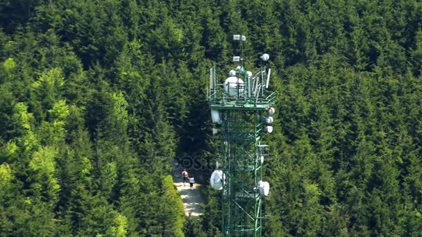 A radio tower in a rural area, surrounded by trees, people walk up a pathway in the background - top view — Stock Video