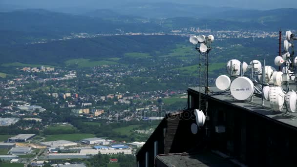 Parabol antenner på taket till en byggnad i ett stort område på landsbygden, en stad och en skog i bakgrunden - ovanifrån — Stockvideo