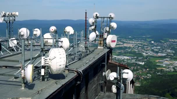 Weiße Parabolantennen auf dem Dach eines Gebäudes, eine Stadt, ein Wald und der blaue Himmel im Hintergrund — Stockvideo