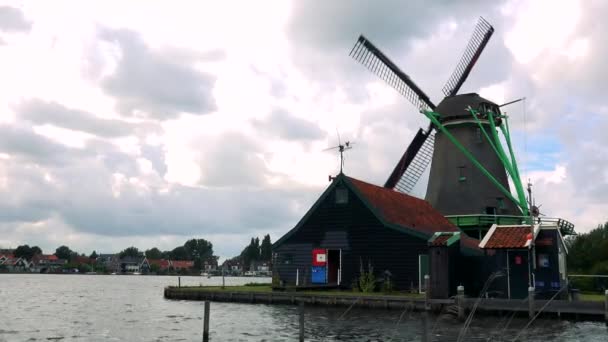 Een windmolen en een huis door een rivier — Stockvideo