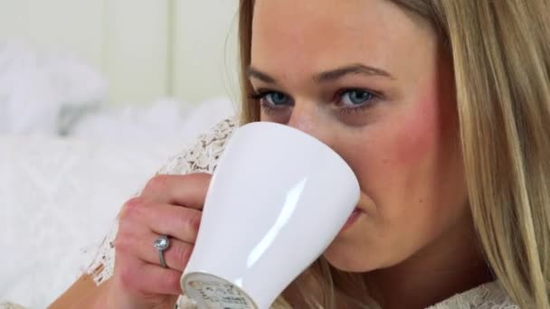 Donna si trova su un letto e beve da una tazza — Video Stock