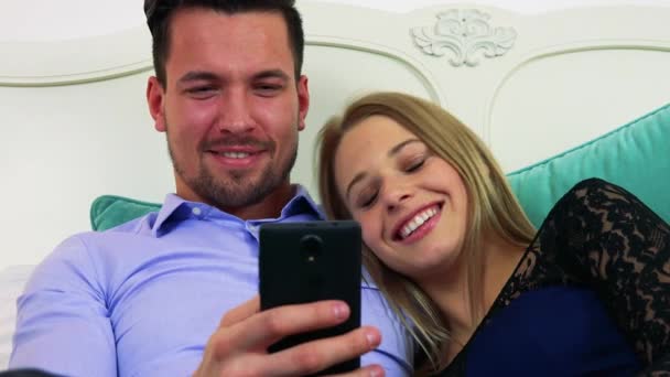 Paar ligt op een bed, hij werkt op een smartphone — Stockvideo