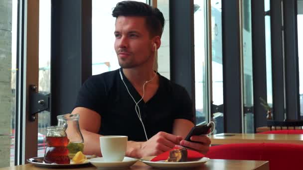 Man in a cafe and listens to music on a smartphone — Stock Video