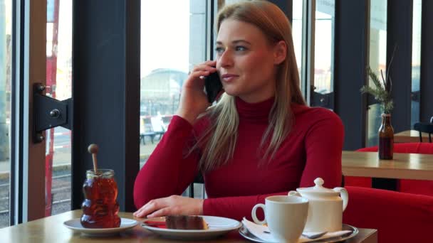 Vrouw in een café gesprekken op een smartphone met een glimlach — Stockvideo