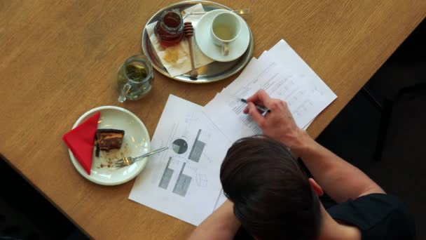 Ein Mann mit Essen in einem Café und erledigt Papierkram — Stockvideo