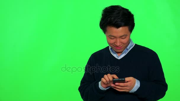 Ασιατική άνθρωπο λειτουργεί σε ένα smartphone με ένα χαμόγελο — Αρχείο Βίντεο