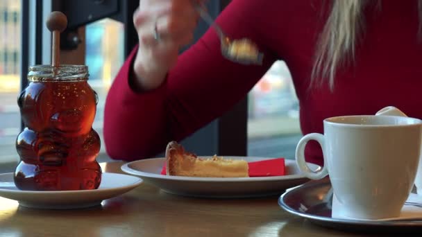 Una mujer se sienta en una mesa en un café y come pastel. — Vídeos de Stock