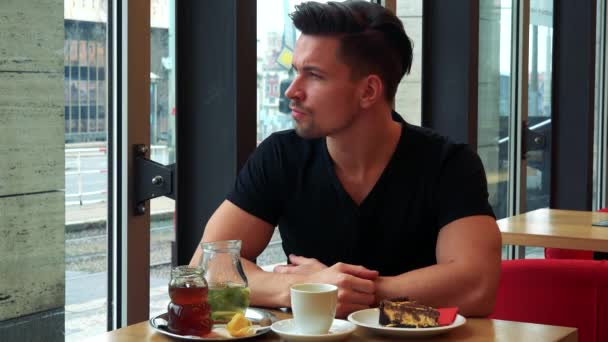 Hombre se sienta en una mesa con comida en un café — Vídeos de Stock