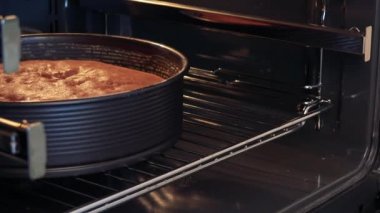 Bir kadın fırın kapağı açık çeker ve pasta denetler 