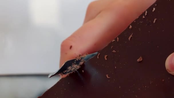Eine Frau reibt eine Tafel Schokolade mit einem Kartoffelschäler — Stockvideo