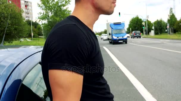 Чоловік стоїть поруч з автомобілем і дивиться навколо — стокове відео