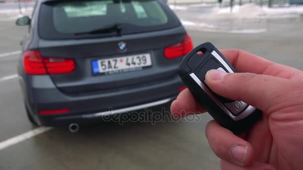 Um homem abre uma bagageira de um carro em um estacionamento com um controle remoto — Vídeo de Stock