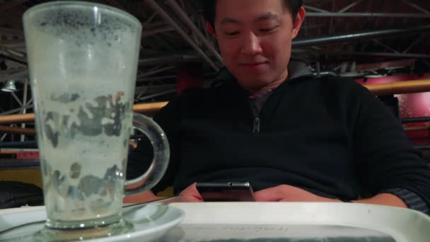 एक कैफे में एक टेबल पर आदमी और एक स्मार्टफ़ोन पर काम करता है — स्टॉक वीडियो