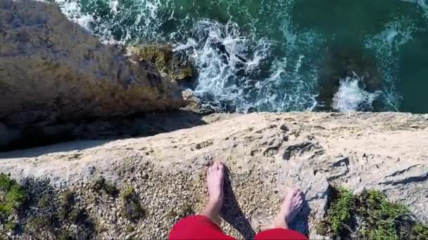 Een man staat op de rand van een klif aan zee — Stockvideo