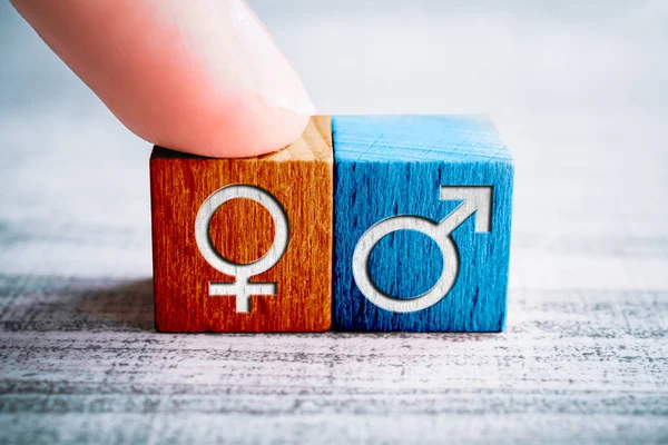 Gender-Symbol für weiblich auf einem Holzblock, der von einem Finger neben dem männlichen Zeichen auf einem Tisch angeordnet ist — Stockfoto