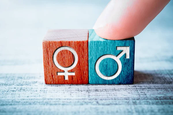 Icona di genere per maschio su un blocco di legno organizzato da un dito accanto al segno femminile su un tavolo — Foto Stock