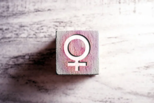 Roze gekleurde geslacht teken voor vrouw op een houten blok op een tafel — Stockfoto