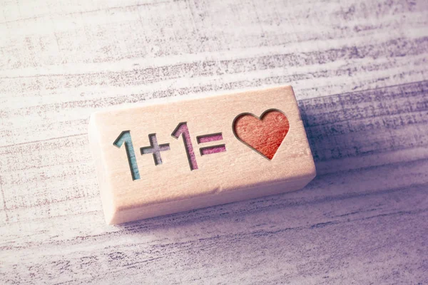 Ecuación 1 más 1 es igual a Corazón como concepto de amor grabado en un bloque de madera en una mesa — Foto de Stock