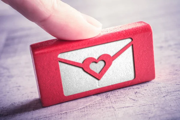 Carta de amor cerrada con un corazón grabado en un bloque de madera roja y arreglado por un dedo femenino en una mesa — Foto de Stock